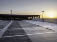 an empty parking lot with buildings and light poles in the background at sunset, in the evening