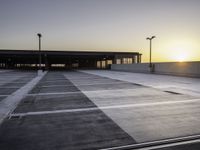 an empty parking lot with buildings and light poles in the background at sunset, in the evening