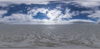 clouds in the sky are reflected by water and snow covered ground, with mountains visible