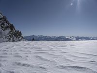 a lone skier sitting on the side of a snow covered slope near a mountain range