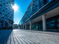 the sun is shining over a modern building near a street with trees and concrete slabs