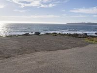 a small road going into the ocean by a shoreline with a bench and surfboards