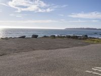 a small road going into the ocean by a shoreline with a bench and surfboards