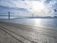 there is a bench on the sand by the water next to a bridge in the distance