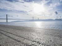 there is a bench on the sand by the water next to a bridge in the distance