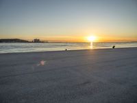 a man riding a skateboard across a sandy beach near the ocean at sunset time