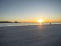 a man riding a skateboard across a sandy beach near the ocean at sunset time