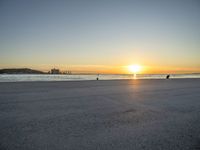 a man riding a skateboard across a sandy beach near the ocean at sunset time