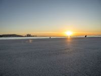 a man riding a skateboard across a sandy beach near the ocean at sunset time