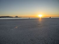 a man riding a skateboard across a sandy beach near the ocean at sunset time