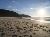 a sandy beach with footprints and waves on a sunny day at the ocean's edge