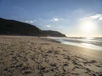 a sandy beach with footprints and waves on a sunny day at the ocean's edge