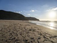 a sandy beach with footprints and waves on a sunny day at the ocean's edge