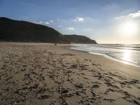 a sandy beach with footprints and waves on a sunny day at the ocean's edge