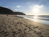 a sandy beach with footprints and waves on a sunny day at the ocean's edge