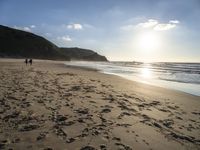 a sandy beach with footprints and waves on a sunny day at the ocean's edge