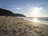 a sandy beach with footprints and waves on a sunny day at the ocean's edge