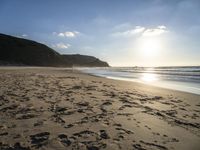 a sandy beach with footprints and waves on a sunny day at the ocean's edge