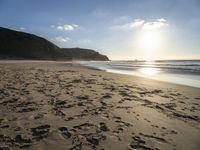 a sandy beach with footprints and waves on a sunny day at the ocean's edge