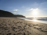 a sandy beach with footprints and waves on a sunny day at the ocean's edge