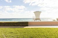 a lawn next to a sandy beach with a lifeguard's chair in the background