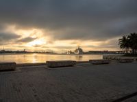 there is a bench on the beach by the water at sunset as a boat sails in the distance