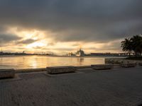 there is a bench on the beach by the water at sunset as a boat sails in the distance