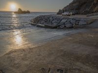 an image of the sun setting over the water and a small beach with rocks on it