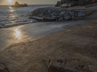 an image of the sun setting over the water and a small beach with rocks on it