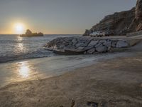 an image of the sun setting over the water and a small beach with rocks on it