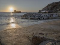 an image of the sun setting over the water and a small beach with rocks on it