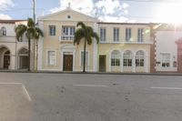 the sun is setting in front of this building and two palm trees are lining the street