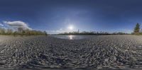 a beach with water near some trees and a sun light over it is shown in a fish - eye picture