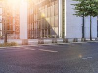 an empty street and two tall buildings with glass windows in the background is sunlight shining down