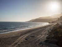 a beach with many small waves on top of it next to a hill side with a sky filled with the sun