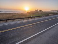 a car drives down the highway in front of the sun setting on the ocean shore