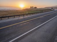 a car drives down the highway in front of the sun setting on the ocean shore