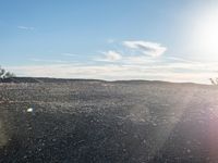 a person on a motorcycle stands in a rocky field as the sun rises behind them