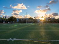 a soccer field is pictured at sunset with the sun glaring behind it and palm trees