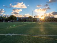 a soccer field is pictured at sunset with the sun glaring behind it and palm trees