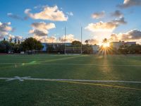 a soccer field is pictured at sunset with the sun glaring behind it and palm trees