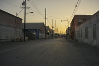 the sun sets behind power lines in an empty alley in a city setting along with a few buildings