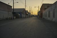 the sun sets behind power lines in an empty alley in a city setting along with a few buildings