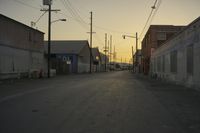 the sun sets behind power lines in an empty alley in a city setting along with a few buildings