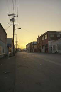 the sun sets behind power lines in an empty alley in a city setting along with a few buildings