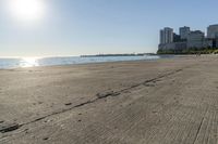 a beach and city skyline with several buildings in the distance and footprints in the sand