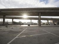 the sun is shining behind a long freeway bridge over highway traffic in a city parking lot