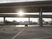 the sun is shining behind a long freeway bridge over highway traffic in a city parking lot