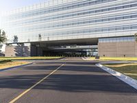 an empty road outside a tall glass building with multiple levels on it's sides