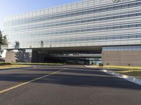 an empty road outside a tall glass building with multiple levels on it's sides